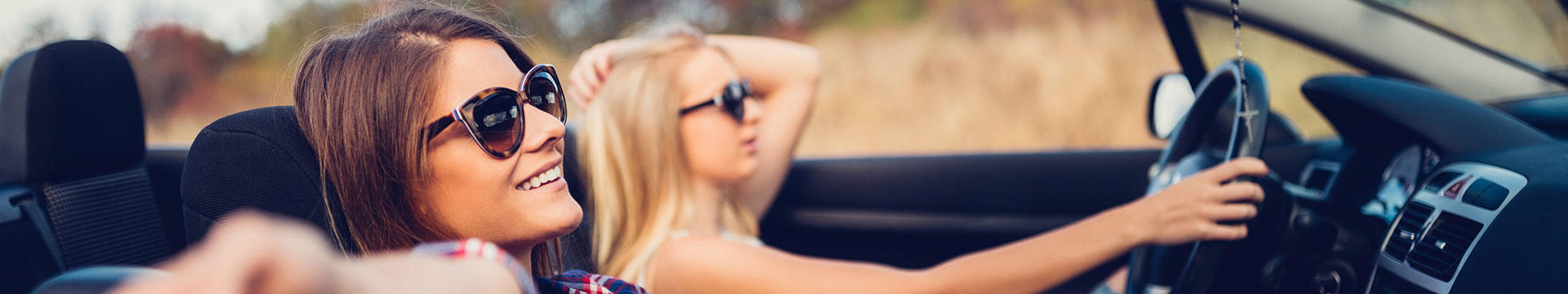 Image of two teen girls wearing sunglasses in the front seat of a convertible car