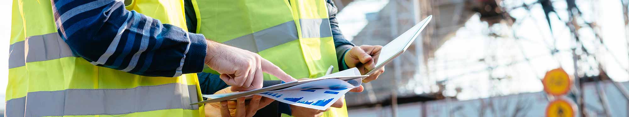 Image of two men in yellow high-visibility vests looking over plans or schematics