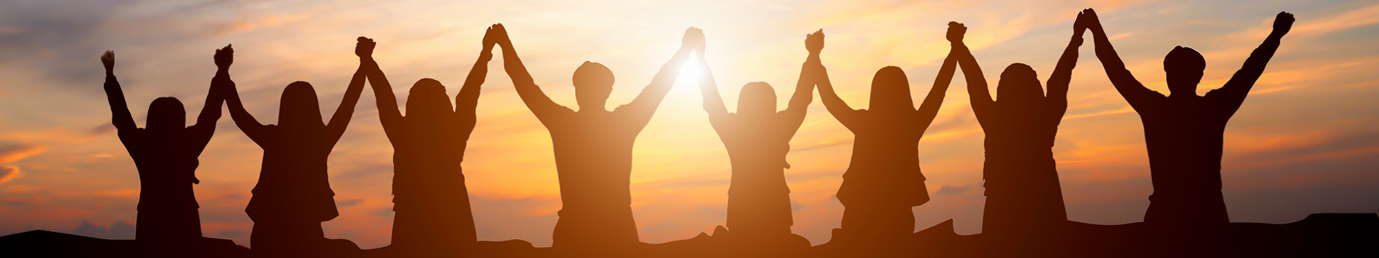 Image of 8 people facing the sunset with their arms raised in the air and their hands clasped together