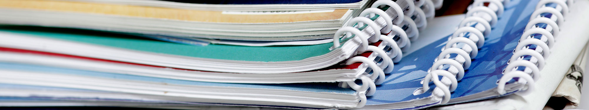 Image of spiral bound manuals with various colored covers stacked upon each other