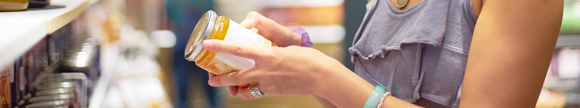 Labeling and Packaging Requirements Banner Image Image of woman reading the label on the back of a jar in a grocery store aisle