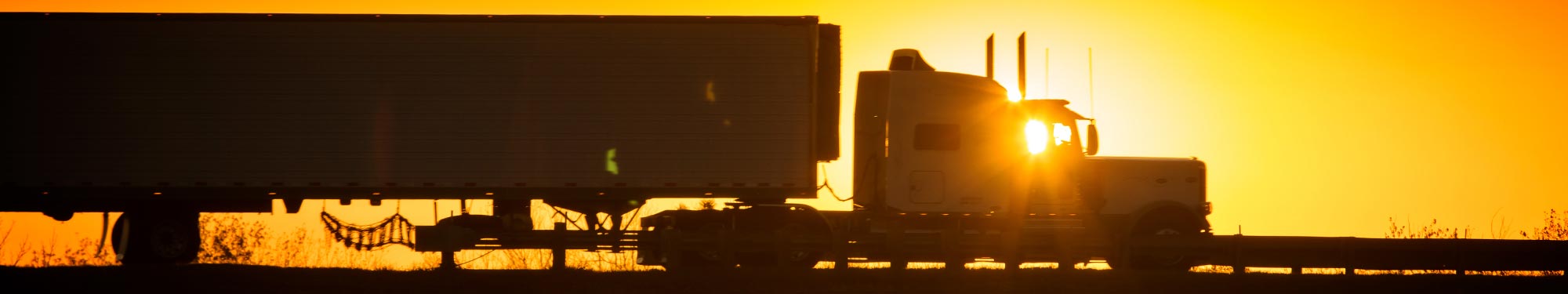 Image of silhouette of semi-truck on a highway as the sun sets