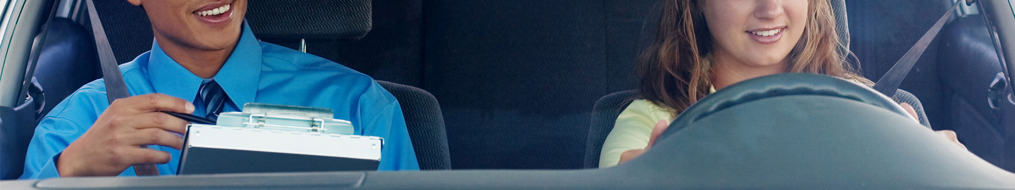 Image of teen girl behind the steering wheel of a car with a driver's education instructor in the front passenger seat