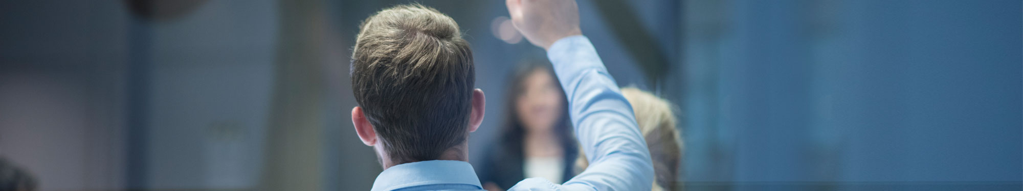 Image of man in a meeting or classroom with his hand raised