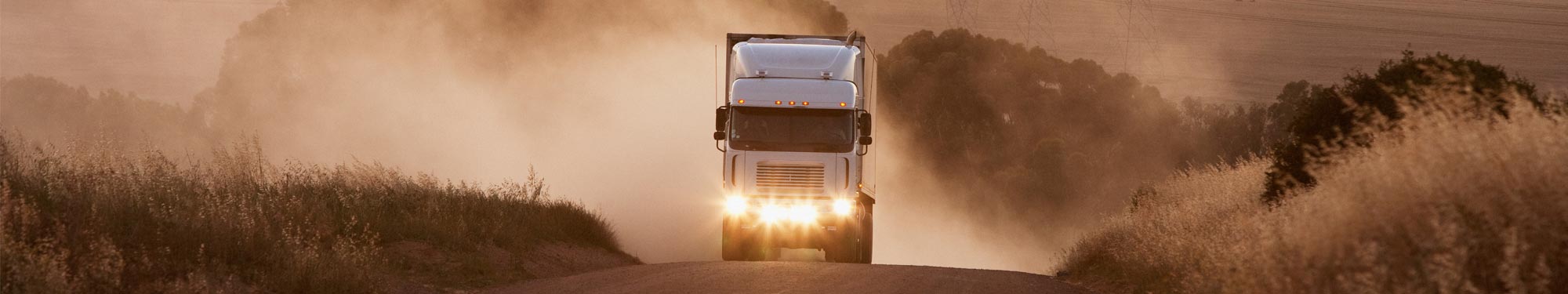 Image of semi-truck driving on a gravel road at dusk with its headlights on
