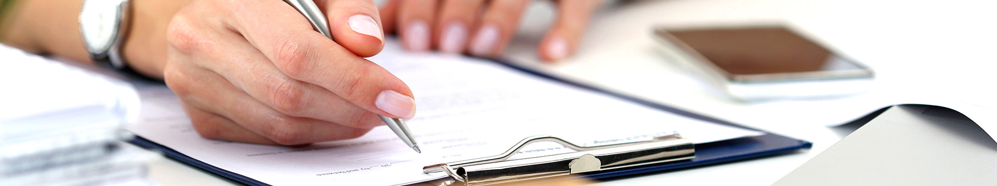 Image of hand holding a pen resting on an application and clipboard