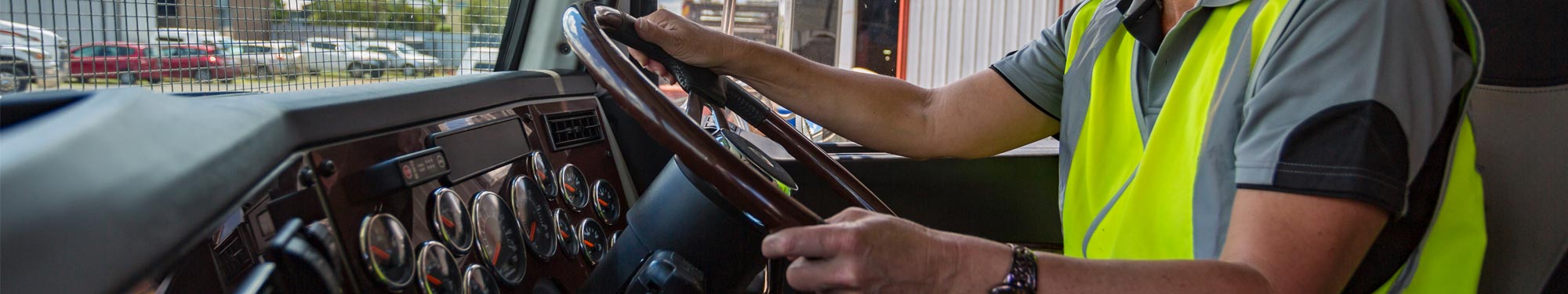 Image of truck driver sitting behind a steering wheel wearing a yellow high-visibility vest