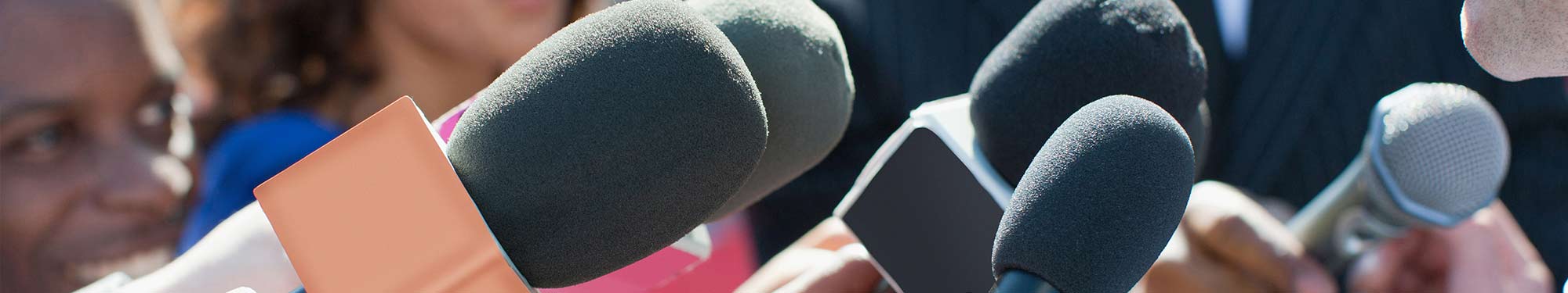 Image of several microphones being held by members of the press as if at a press conference