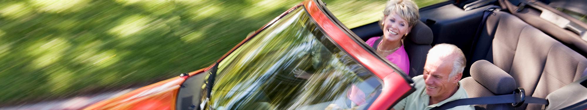 Image of senior couple in the front seat of a convertible car as it drives down the road