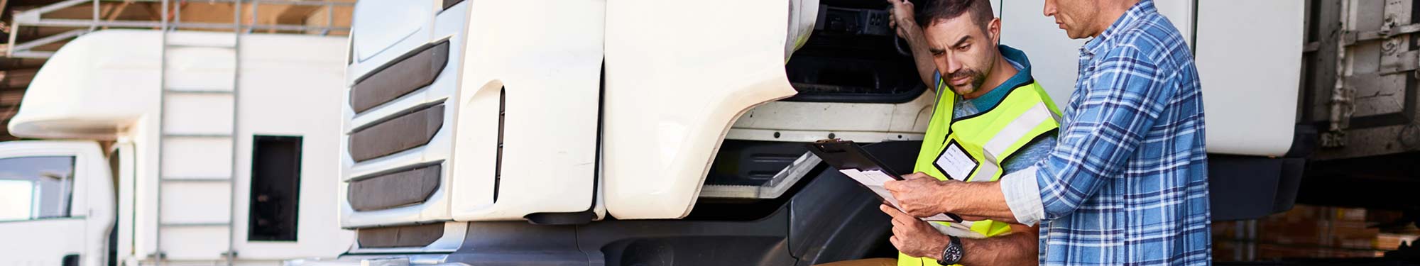 Image of two men standing outside a semi truck looking a paperwork with the driver's side door open