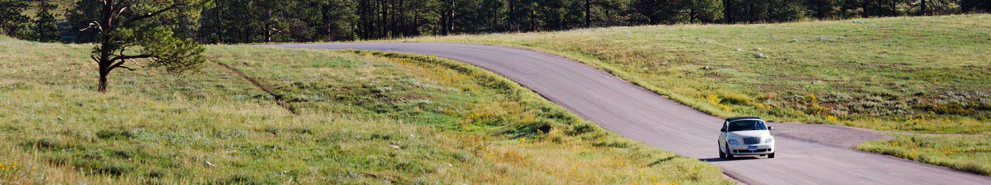 Image of convertible car with the top up driving on a paved road through the countryside