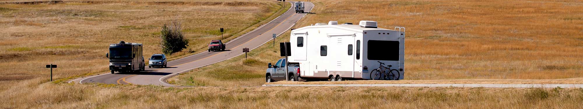 Image of campers and vehicles driving on a winding road through the prairie of South Dakota