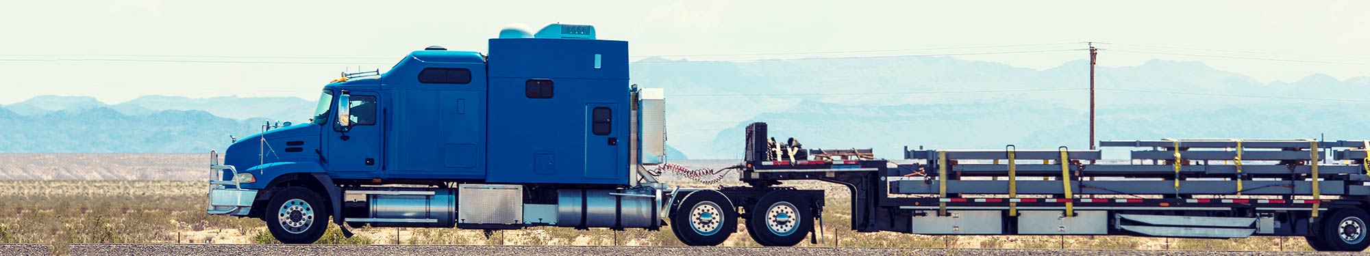 Image of blue semi tractor with loaded flatbed trailer